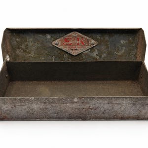 May include: A rectangular metal tool box with a weathered, dark gray finish and an open lid. A diamond-shaped metal plate is attached to the interior lid, featuring the red and white text S-K TOOLS, THE SHERMAN-KLOVE CO, CHICAGO, ILL, U.S.A.