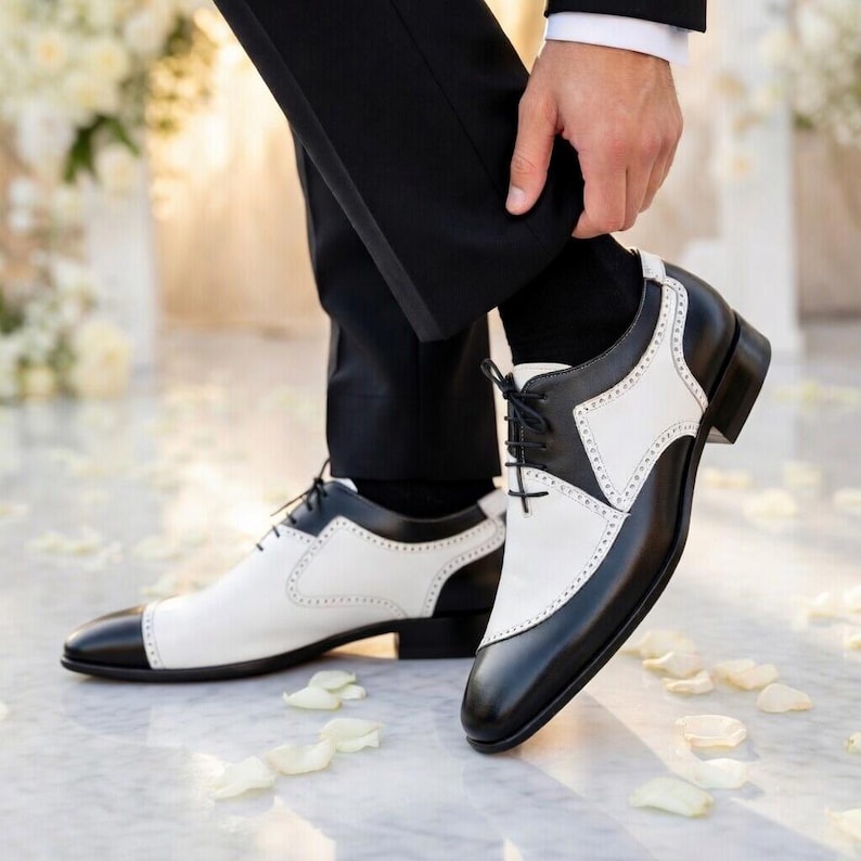 May include: Two-tone black and white dress shoes with a classic design. The shoes feature a black toe cap, heel, and trim, with white panels and decorative perforations. The shoes are laced up and appear to be made of leather. The image shows the shoes from a low angle.