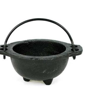 May include: A small, black cast iron cauldron with a curved handle. The cauldron has three small feet and a rounded bowl shape. The handle is attached to the sides of the cauldron.