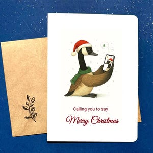 May include: A Christmas card with a goose wearing a Santa hat and green scarf, holding a phone. The card reads "Calling you to say Merry Christmas". A kraft paper envelope with a leaf design is included.