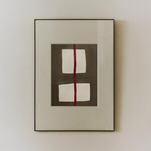 May include: Framed abstract art print featuring two white rectangular shapes stacked vertically, bisected by a vertical red line. The background is a muted brown, and the frame is a neutral off-white with a black border.