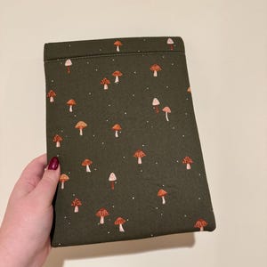 May include: A dark green fabric case with a repeating pattern of orange and white mushrooms and small white dots. The case is rectangular and appears to be a sleeve for a tablet or e-reader.
