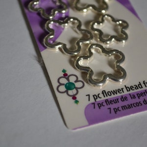May include: A package of seven silver flower bead frames. The package is purple and white with the text "7 pc flower bead frames", "7 pc fleur de la perle carrés", and "7 pc marcos de flor".
