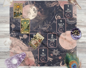 May include: A celestial-themed tarot spread with a navy and blush pink patterned cloth. Tarot cards are laid out, including "The Star" and "The Empress". Additional items include crystals, a peacock feather, and a bundle of sage. The layout is on a light wood surface.