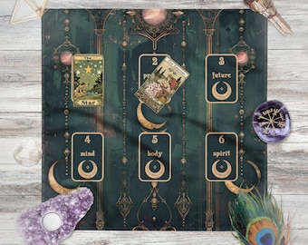 Op de afbeelding: Een teal en gouden tarotdoek met een hemels ontwerp, met tarotkaarten en halve manen. De doek bevat de kaarten "The Star" en "The Empress". Extra items zijn kristallen, een veer en een smudge stick.