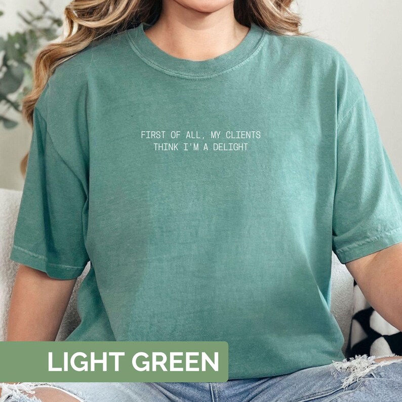 Puede incluir: Camiseta verde claro con el texto blanco "FIRST OF ALL, MY CLIENTS THINK I'M A DELIGHT". La camiseta es de color verde claro liso y tiene mangas cortas.