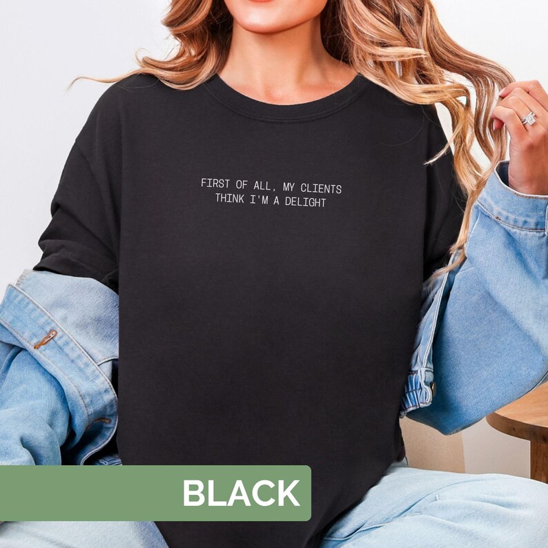 Puede incluir: Camiseta negra de cuello redondo con el texto blanco "FIRST OF ALL, MY CLIENTS THINK I'M A DELIGHT". La palabra "BLACK" se muestra en un rect&aacute;ngulo verde en la parte inferior de la camiseta.