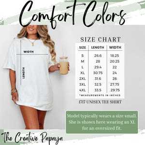 Puede incluir: Una camiseta unisex blanca con el texto "Comfort Colors" en una fuente cursiva. Una tabla de tallas muestra las medidas en pulgadas para las tallas S a 4XL. La modelo lleva una XL para un ajuste oversize. The Creative Papaya.
