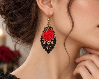 May include: A dangling earring featuring a central bright red fabric rose surrounded by intricate black lace detailing and antique brass-toned metal filigree. The earring hangs from a simple brass hook and displays a teardrop-shaped silhouette.