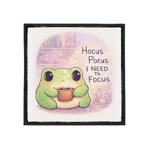 May include: Square patch with a black border. It features a cartoon frog holding a mug of coffee. The frog is light green with large black eyes. Text reads "Hocus Pocus I NEED TO Focus" in black letters.