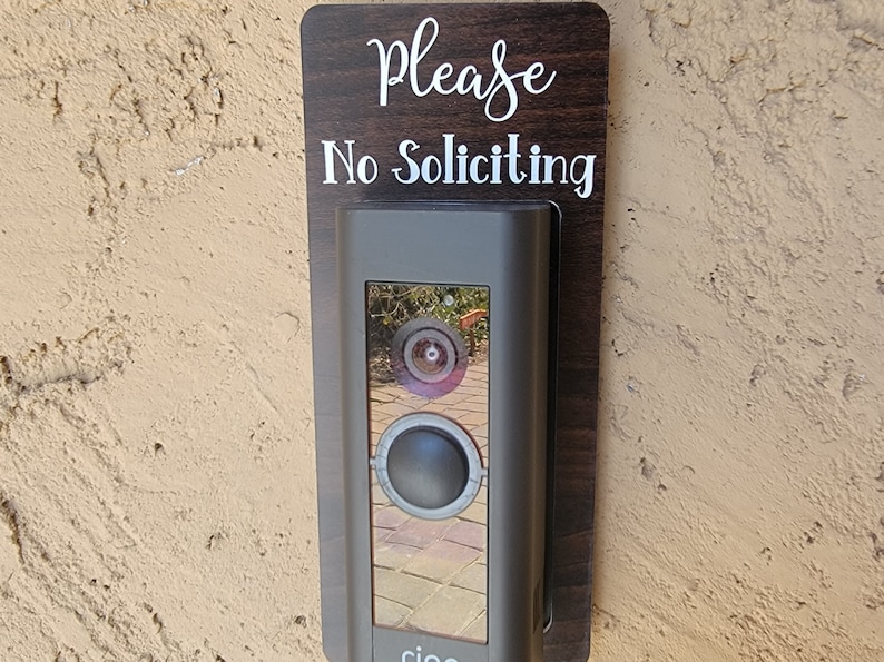 Ring doorbell with laminate wood grain sign around stating Please No Soliciting