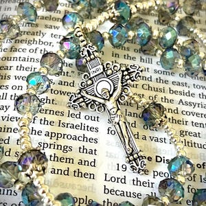May include: A rosary with iridescent blue and gray faceted beads and silver-toned accents. The centerpiece is a detailed crucifix with the letters INRI. The beads are strung on a silver-toned chain, creating a religious accessory.