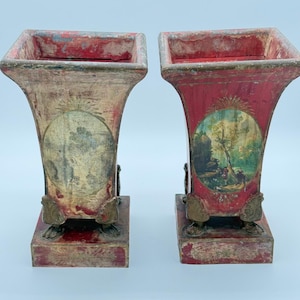 May include: Pair of antique decorative vases with a square top and flared body. One vase is painted red, the other is a faded beige. Each vase features a painted oval scene and ornate metal accents.