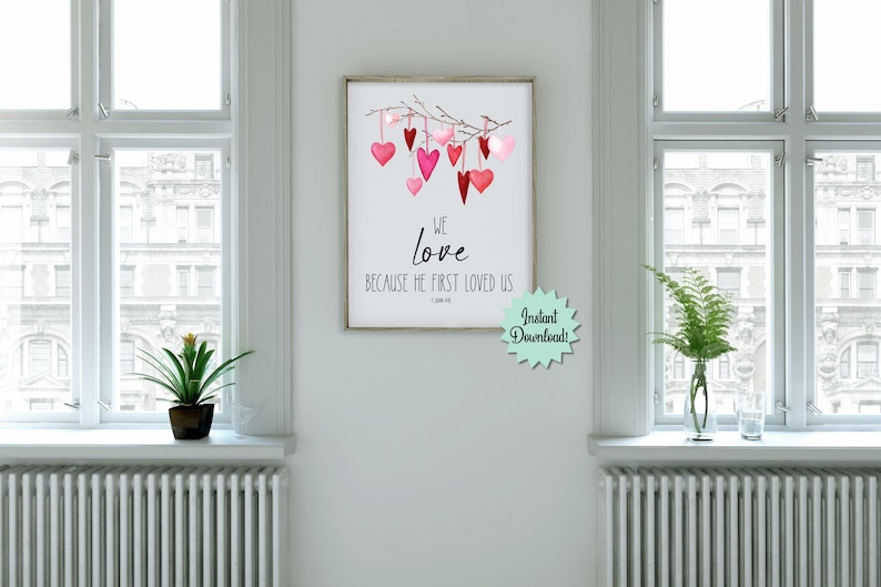 May include: Printable wall art with a watercolor illustration of a branch with pink and red hearts hanging from it. The text reads "We love because He first loved us - 1 John 4:19".