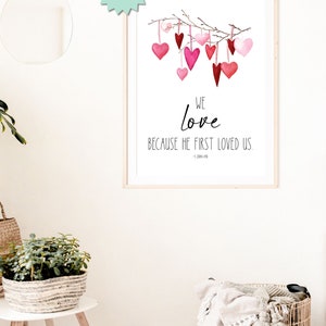 May include: Printable wall art with a watercolor illustration of pink and red hearts hanging from a branch. The text reads "We love because he first loved us. - 1 John 4:19"