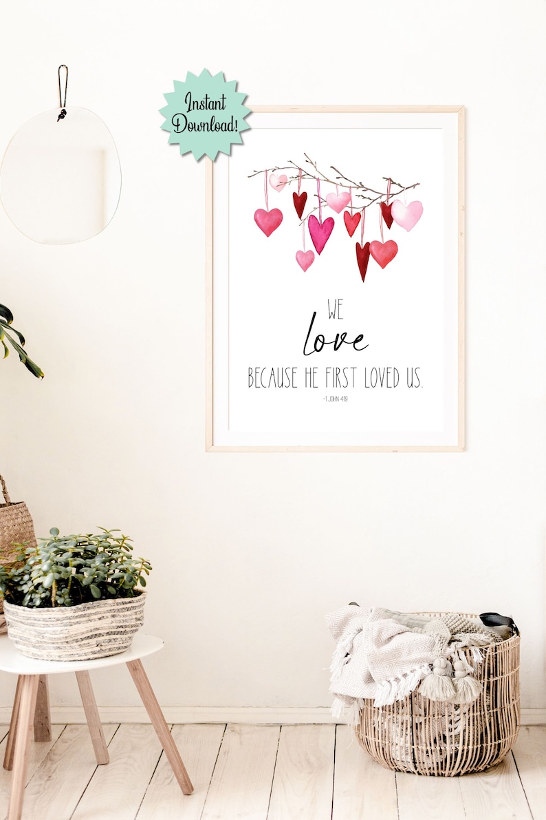 May include: Printable wall art with a watercolor illustration of pink and red hearts hanging from a branch. The text reads "We love because he first loved us. - 1 John 4:19"