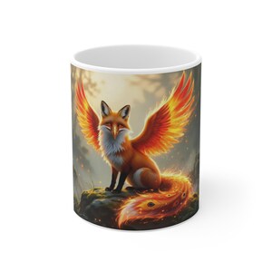 Peut inclure: Mug en céramique blanche avec une illustration fantastique d'un renard avec des ailes et une queue orange et jaune flamboyantes. Le renard est perché sur un rocher moussue sur un fond de forêt flou. La tasse a une capacité standard de 325 ml.