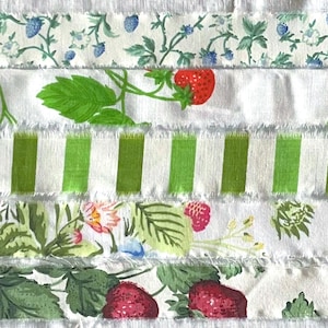 May include: Five horizontal strips of fabric with frayed edges arranged in a stack. The patterns include blue berries on vines, red strawberries with green leaves, vertical lime green and white stripes, mixed floral prints, and large red strawberries.