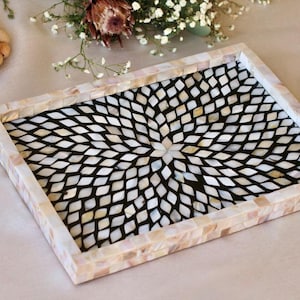 May include: Rectangular decorative tray with a mother-of-pearl mosaic design. The tray features a black interior with a white diamond pattern, framed by a mosaic border. The tray is a decorative item.