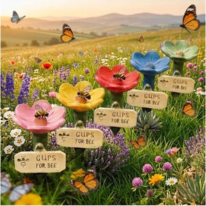 Puede incluir: Una escena de jardín vibrante presenta bebederos para abejas con forma de flor de colores con el texto "CUPS FOR BEE". Hay abejas y mariposas presentes. Los bebederos con forma de flor son de color rosa, amarillo, rojo, azul y verde.