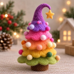 Puede incluir: Un adorno de árbol de Navidad de fieltro de aguja en forma de cono con un degradado de colores desde el morado en la parte superior hasta el verde en la base. El árbol está decorado con pequeñas bolas de fieltro redondas y una estrella amarilla.