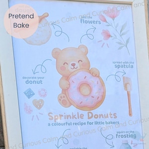 May include: A framed instructional poster titled Sprinkle Donuts, a colourful recipe for little bakers. It features a central light brown teddy bear holding a pink frosted donut, surrounded by illustrations of a spatula, flowers, and text.