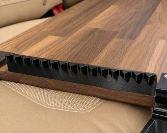 May include: A rectangular wooden board featuring a dark brown wood grain pattern, equipped with a black plastic attachment along one edge. The attachment has a series of evenly spaced, triangular teeth protruding upwards along its entire length.