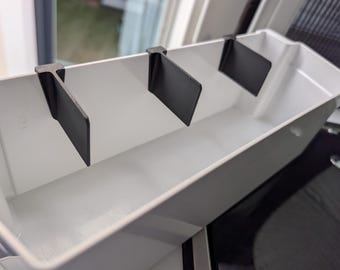 May include: A white plastic container with three black dividers. The dividers are evenly spaced and attached to the inside of the container. The container is rectangular and has a smooth, clean surface.