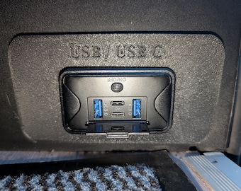 May include: A black USB charging station with the text "USB / USB C" above the ports. The station has two blue USB 3.0 ports, two USB-C ports, and an on/off button. The ports are labeled "PD" and "DC3.0".