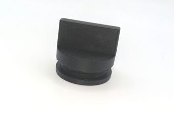 May include: A matte black plastic knob featuring a flat, rectangular top handle section and a circular base. The component has a textured surface finish and a distinct stepped design, showing a cylindrical lower portion beneath the wider top grip.