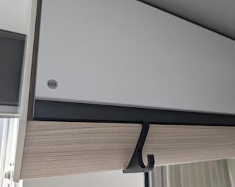 May include: Close-up of a cabinet with a light wood grain drawer front and a white cabinet door. A black hook is attached to the drawer. The word "PUSH" is printed on a small, round, silver button on the cabinet door.