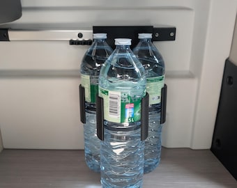 May include: Three clear plastic water bottles, each holding 1.5 liters, are held in a black metal bracket. The bottles are filled with clear liquid and have white caps and green and white labels. The bracket is mounted on a light-colored surface.