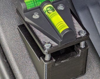 May include: A black, 3D-printed level with two green and yellow bubble vials. The level is mounted on a black base and secured with silver screws. The vials are filled with a bright green liquid.