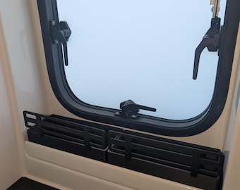 May include: Interior view of a window with a black frame and a black folding shade. The window is open, revealing a light blue sky. The shade is folded and sits above a white ledge.