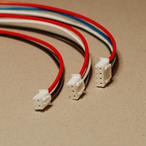 May include: Three electrical wire assemblies featuring multi-colored insulated cables in red, white, black, and blue. Each cable terminates in a white plastic connector housing with four visible metal pin slots for electronic connectivity.