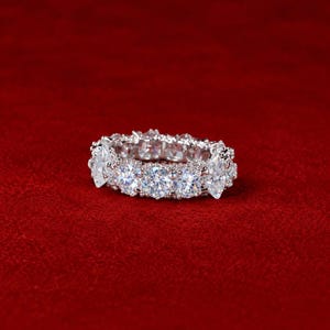 May include: A silver-toned eternity band ring featuring a repeating pattern of alternating round-cut and marquise-cut clear stones set in a metallic frame. The ring displays a continuous arrangement of faceted gems that catch the light.