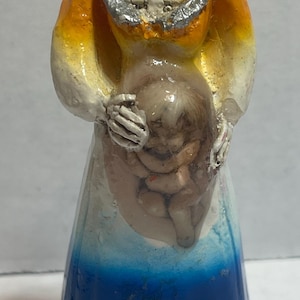 May include: A painted figurine of a skeletal figure wearing a hooded robe. The figure holds a fetus-like form. The robe transitions from orange to white and blue. The figure's skull and ribcage are visible.