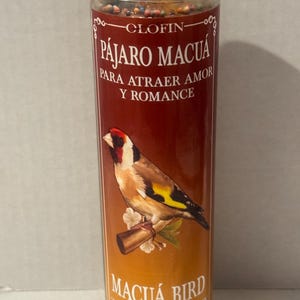Puede incluir: Vela de vidrio cilíndrica con un fondo degradado rojo y naranja. La vela presenta una ilustración detallada de un pájaro posado en una rama, con texto en español e inglés: "Pájaro Macuá" y "Macuá Bird" para atraer el amor y el romance.