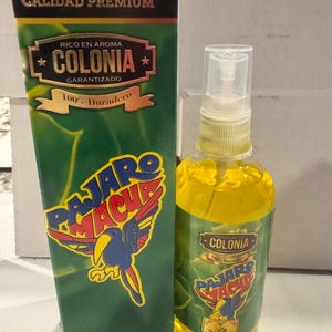 Puede incluir: Una botella de colonia líquida amarilla y su caja a juego. La caja y la botella presentan una etiqueta verde y dorada con las palabras "COLONIA" y "PAJARO MACHU". La botella contiene 100 ml de spray natural.