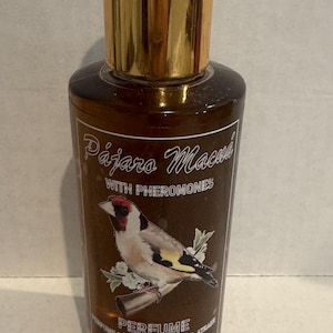 Puede incluir: Botella de perfume marrón con tapón dorado. La etiqueta presenta el texto "Pájaro Macuá" y una ilustración detallada de un pájaro. La botella también incluye las palabras "with pheromones" y "perfume".