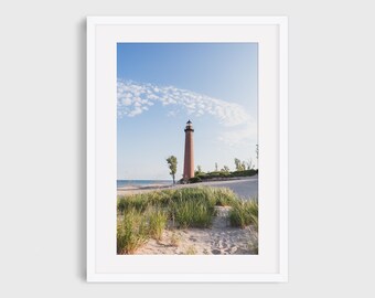 May include: A framed photograph of a lighthouse on a sandy beach under a blue sky with wispy clouds. The lighthouse is tall and brick-colored, with a black top. Green grass and a few trees are in the foreground. The text "Frame and mat for example only. This listing is for an unframed In This Instance Photography print." is at the top.