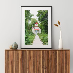 May include: A framed photograph of a white house with a red roof and a wooden walkway leading to the front door. The house is surrounded by green trees and bushes.