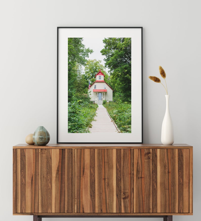 May include: A framed photograph of a white house with a red roof and a wooden walkway leading to the front door. The house is surrounded by green trees and bushes.