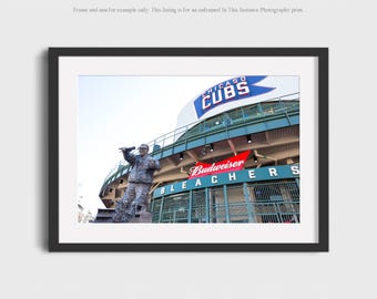 May include: A photograph of a statue of a man holding a microphone in front of the Chicago Cubs stadium. The stadium has a green exterior with a red Budweiser sign and the words "BLEACHERS" in white letters. The sign above the stadium reads "CHICAGO CUBS" in blue letters.