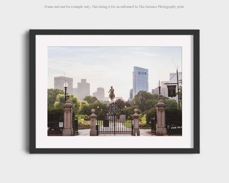 May include: A photograph of a wrought iron gate leading into a park with a statue of a man on horseback in the background. The park is surrounded by trees and buildings. The sky is a light blue with some clouds.