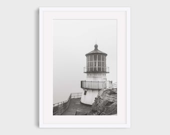 May include: Black and white photograph of a lighthouse on a rocky cliff, framed in white. The lighthouse has a cylindrical tower with a lantern room and a railing around the top. The text "Frame and mat for example only. This listing is for an unframed In This Instance Photography print." is at the top.