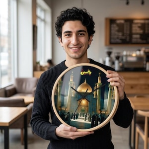 May include: A round wall clock with a light wood frame featuring a printed image of a golden domed mosque with tall minarets and a crowd of people in front. The clock has black hour, minute, and second hands and includes red and yellow text.