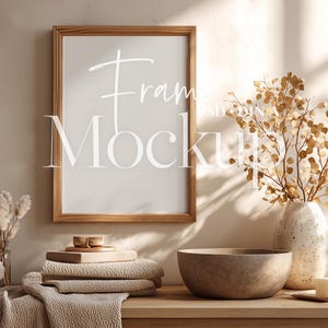 Może przedstawiać: Drewniana makieta ramy ze słowem "Frame Mockup" w białym skrypcie. Rama jest wyświetlana na drewnianym stole z elementami dekoracyjnymi, w tym wazonem z suszonymi gałęziami, miską, ręcznikami i dozownikiem mydła.