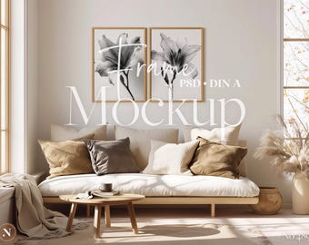 May include: Two rectangular wall frames with light wood borders containing black and white floral prints. The text Frame PSD DIN A Mockup is overlaid in white. The frames are positioned above a low sofa with beige and brown cushions.