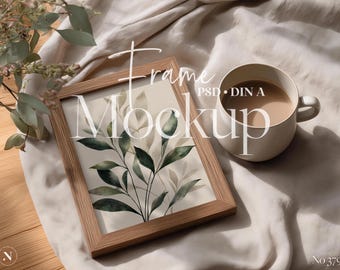 May include: A wooden framed print with a botanical illustration of green and beige leaves. A white mug filled with a light brown liquid sits next to the frame. The words "Frame Mockup" are written on the image.
